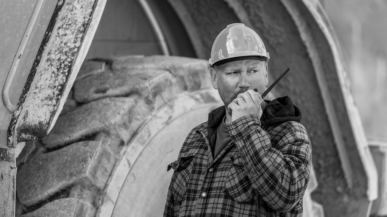 Mining worker in hardhat on the phone in front of gigantic mine truck